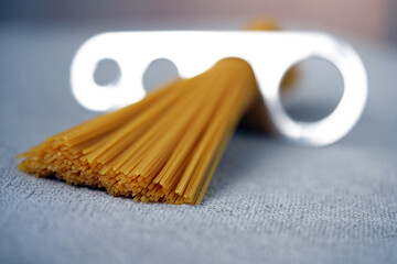A measure of spaghetti with pasta in it lying on a black background. Close up.  Cooking. Metal kitchen tools. Batch measurement. Kitchenware. Pasta. Italian Cuisine                                    