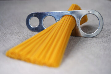 A measure of spaghetti with pasta in it lying on a black background. Close up.  Cooking. Metal kitchen tools. Batch measurement. Kitchenware. Pasta. Italian Cuisine                                    