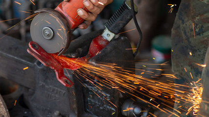 Young workers use metal grinders Steel parts of a motorbike To design and modify Beautiful orange sparkle from metal grinding.