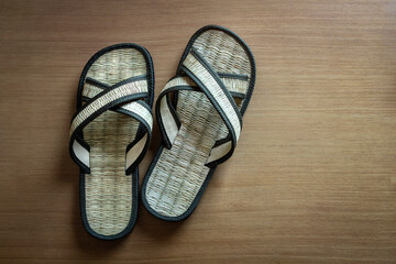 Handmade woven slipper made of grass on wooden floor, top view, Thailand