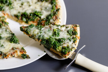Sliced fresh baked vegetarian pizza with spinach and mozzarella with a pizza cutter.