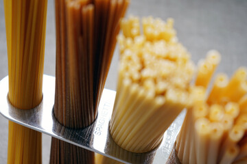 A measure of spaghetti with pasta in it lying on a black background. Close up.  Cooking. Metal kitchen tools. Batch measurement. Kitchenware. Pasta. Italian Cuisine                                    