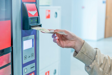 Woman inserts a 100 ruble banknote into a currency validator to pay for her drink at a vending coffee machine. Close-up view. 24-7 store. Selective focus. Small business theme.