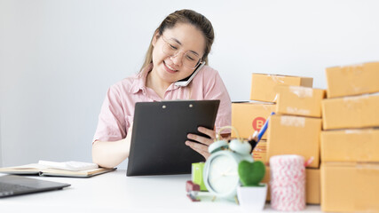 Naklejka premium Young woman selling products online was talking on the phone to receive an order from a customer who called and wrote down the list in a notebook, New kind of business for young, Sell online.