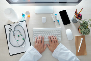 Hands of doctor working on computer at his office desk, view from above