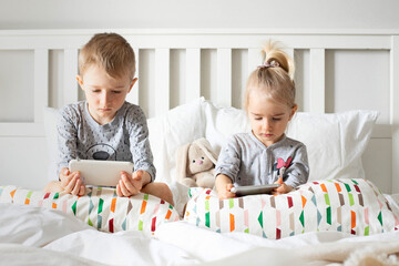 Fototapeta premium Children brother and sister watch cartoons, play on the phone, smartphone on the bed.