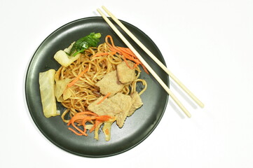 fried yakisoba Japanese noodles slice pork and cabbage with carrot eat by wooden chopsticks on plate