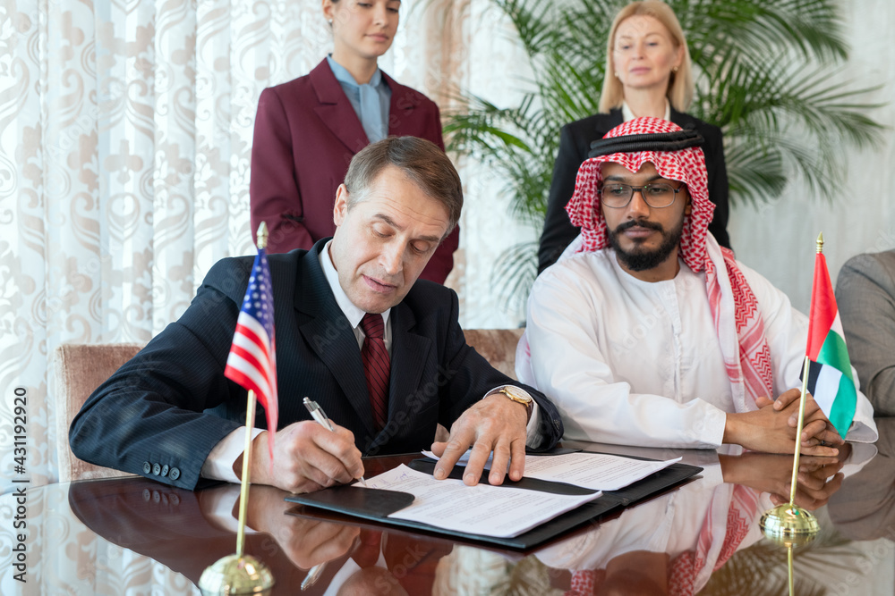 Aufkleber a group of people sitting by table while one of them signing contract after negotiation