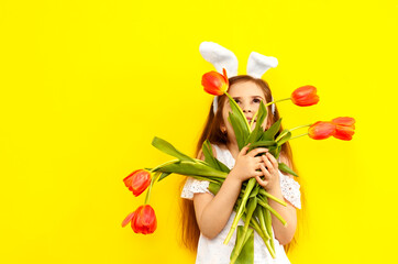 Excited girl in bunny bunny ears on her head on a yellow background. Cheerful playful smiling happy child with a bouquet of tulip flowers. Easter and spring