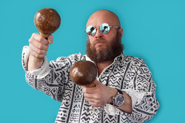 A guy with a bald head in glasses with maracas in his hands. A musician with a full beard and a mustache in a colorful shirt. Man portrait. Coconut Musical Instrument
                               