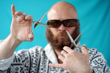Tailor. A man with a beard holds a scissor in his hands. Guy with glasses portrait. Boy with a bald head in a colorful shirt. The hairdresser                                                           
