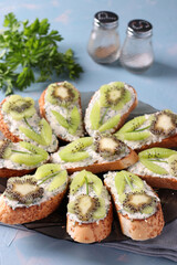 Homemade sandwiches with kiwi, cream cheese and garlic on a plate on light blue background.
