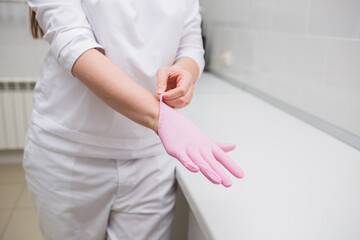 close-up of the doctor's hands putting on pink disposable gloves in the clinic room