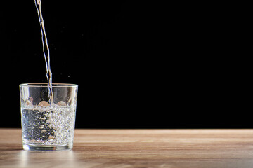 glass tumbler filling with water on table with black background
