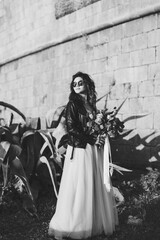 Black and white photo of bride in sunglasses with a bouquet of flowers against the background of the castle wall and agave