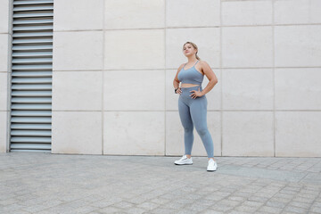 Fototapeta na wymiar Pretty fit young plus size woman in sports bra and leggings standing outdoors after jogging