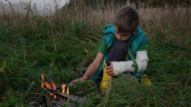 blond boy with bandaged hand looks at fire