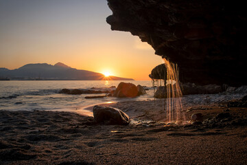 Waterfall falling onto a beach from a stone at sunset. Ceuta coast in Spain.
