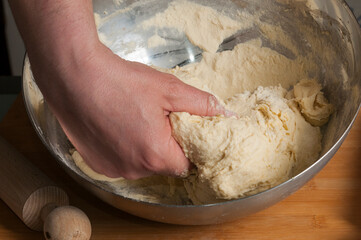 Man kneads bread dough on a wooden pastry board