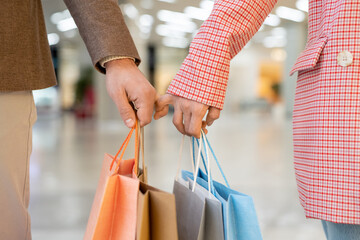 Young couple in casualwear holding paperbags while moving along mall