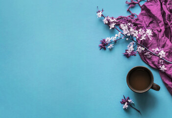 A cup of hot morning coffee and blossoming cherry branches on a blue background. View from above. Close up concept of holidays and good morning wishes. 