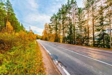 Turn the country broken road. Mixed forest. Sunset over the forest lake. Autumn weather. Beautiful nature. Russia, Europe. View from the side of the road.