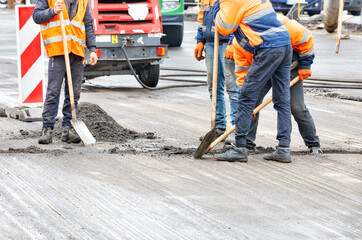 Road workers are shoveling the old road surface on the roadway.