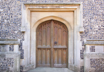 Fototapeta na wymiar Old wooden door to Christian church embedded in flint stone wall