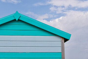 Turquoise and white wooden beach hut against blue and white cloudy sky