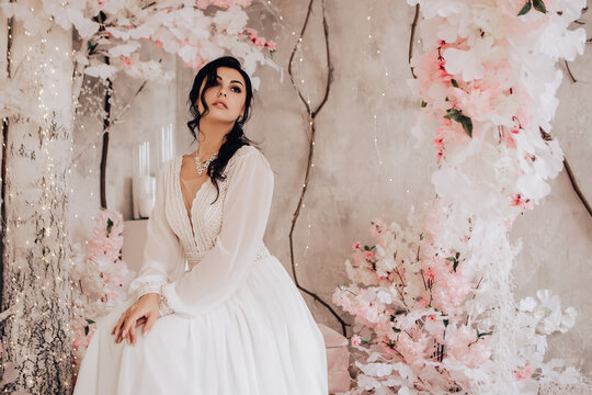 Woman married bride celebrate engagement. Pink wedding photo zone in studio made of white flowers. Place for making pictures. Procreation romantic amazing woman indoor, copy space.
