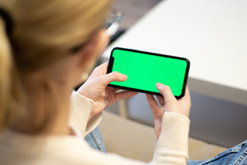 Woman at home using smartphone with green mockup screen. Girl gamer mobile phone. Point of view shot