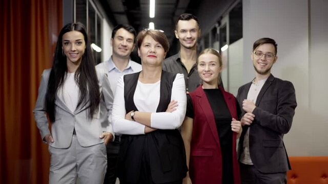 Group of Caucasian coworkers posing in office corridor. Confident successful men and women looking at camera smiling standing at workplace. Teamwork and team spirit concept