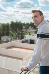An attractive adult Caucasian man looking at the horizon from a balcony with the sky out of focus in the background. vertical photo