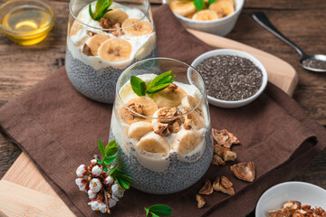 Healthy dessert with chia seeds and coconut milk with banana, honey and nuts on a wooden brown background. Side view, close-up.