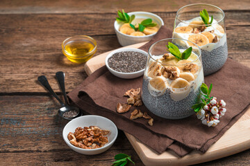Healthy pudding with coconut milk, chia seeds, banana, nuts and honey on a brown background. Side view with copy space.
