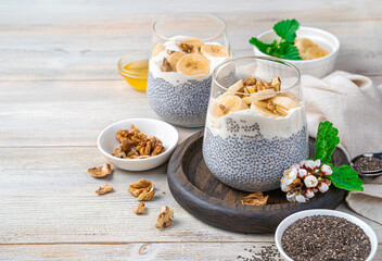 A healthy, vitamin-rich dessert with chia seeds on a light background with space to copy. It is made from chia seeds and coconut milk with the addition of banana, honey and nuts.