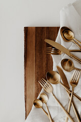Golden plated metal cutlery on linen napkin and wooden board. Top view, flat lay image. 