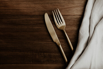 Golden plated fork and knife on brown wooden table. Flat lay, top view image. 