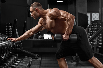 Muscular man working out in gym doing exercise for back. Single arm dumbbell row