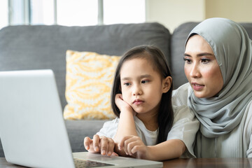Young mother using laptop with her daughter on her lap Homeschool virtual internet online class
