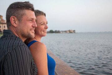 Young Beautiful Couple Profile Smiling Standing Together Looking Out Over Bay at Sunset