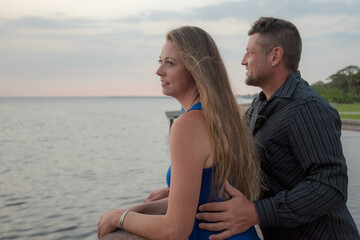 Young Charming Couple Standing Closely Together Looking over the Water at Sunset