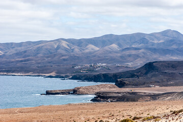 Landscape with yellow send, white clouds, blue sea and mountain peaks in natural park of Jandia