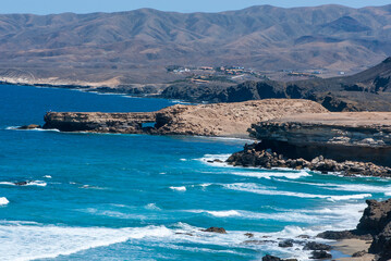 Landscape with yellow send, blue sea, big white waves, sea steep cliffs and mountain peaks in nature park of Jandia