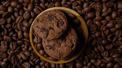 A stack of chocolate cookies inside wooden bowl around arabian coffee beans in white background
