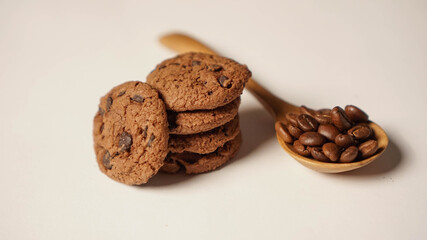 A stack of chocolate cookies beside a spoon of brown coffee beans in white background