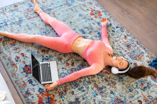 Woman lying with eyes closed on at home during online yoga class. Relaxation after training with soothing music.