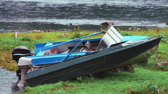 Two motorboats made of iron on the shore. Each of them has its own engine. And one of them also has oars. The boats have seats for passengers and the captain. There is water around the boats.