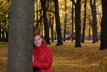 A girl stands near a tree against the background of fallen autumn foliage