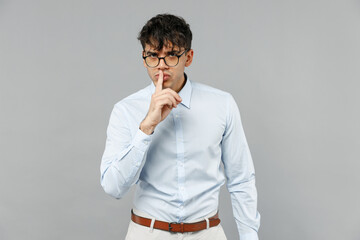 Young secret fun employee business latin man 20s corporate lawyer in classic white shirt glasses say hush be quiet with finger on lips shhh gesture isolated on grey color background studio portrait.